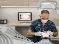 Dentysta w masce i rękawiczkach bada usta pacjenta.