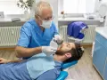 Dentysta w niebieskim fartuchu bada zęby pacjenta. Szukasz miejsca, gdzie wyrwać zęba na NFZ?