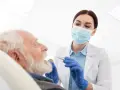 Dentystka w masce bada zęby starszego mężczyzny przy użyciu narzędzi stomatologicznych.