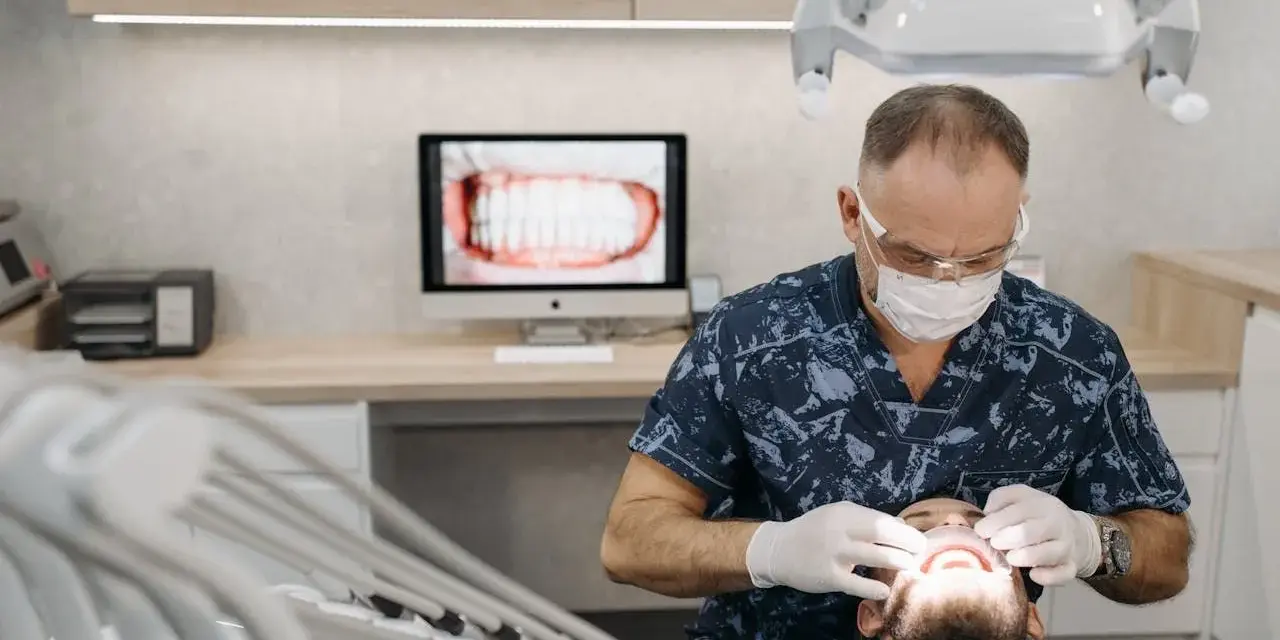 Dentysta w masce i rękawiczkach bada usta pacjenta.