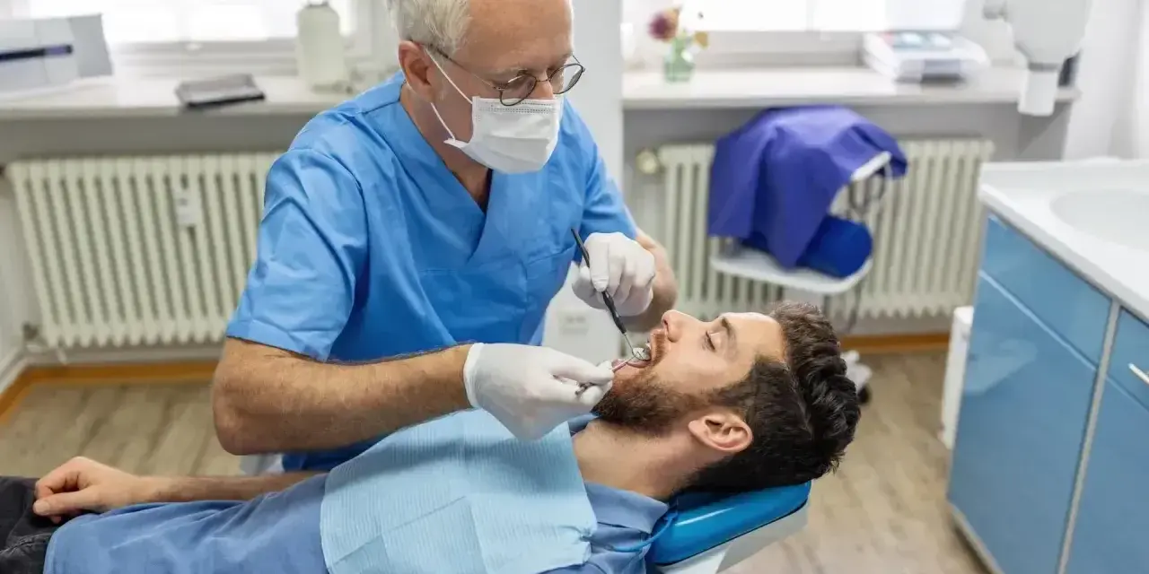 Dentysta w niebieskim fartuchu bada zęby pacjenta. Szukasz miejsca, gdzie wyrwać zęba na NFZ?