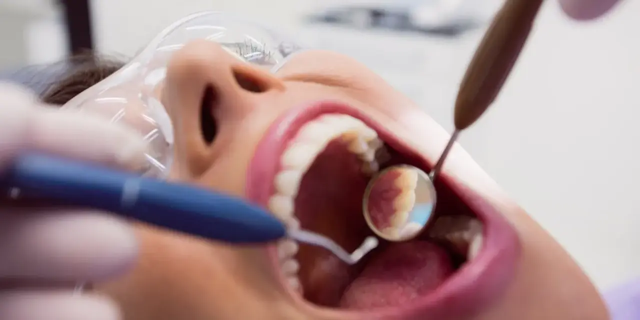 Pacjentka u dentysty, zastanawia się, czy piaskowanie zębów boli. Widać narzędzia stomatologiczne i otwarte usta.