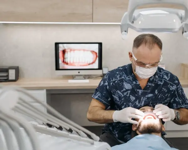 Dentysta w masce i rękawiczkach bada usta pacjenta.