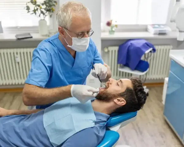 Dentysta w niebieskim fartuchu bada zęby pacjenta. Szukasz miejsca, gdzie wyrwać zęba na NFZ?