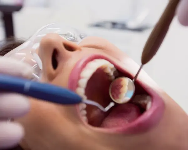 Pacjentka u dentysty, zastanawia się, czy piaskowanie zębów boli. Widać narzędzia stomatologiczne i otwarte usta.