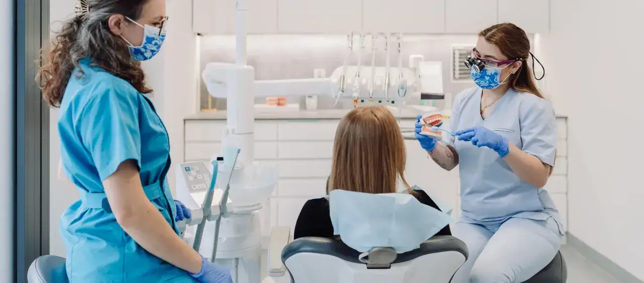 Dentystka pokazuje pacjentce model szczęki, wyjaśniając, ile trwa higienizacja.