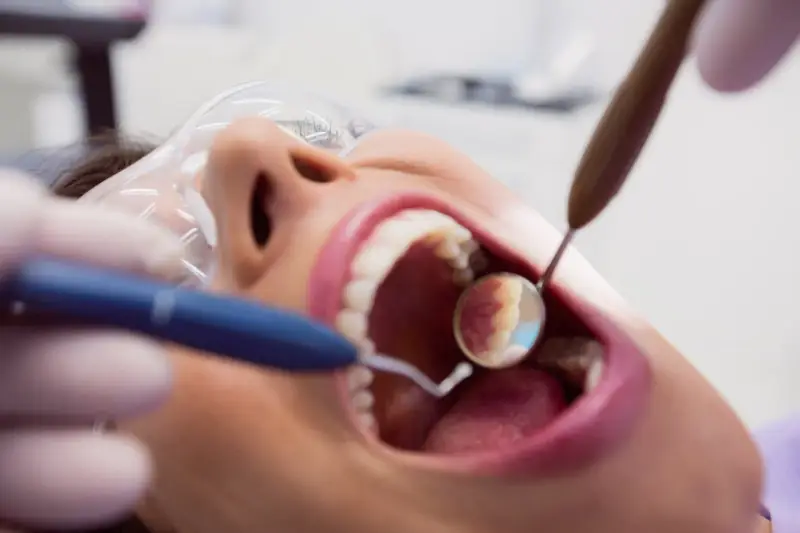 Pacjentka u dentysty, zastanawia się, czy piaskowanie zębów boli. Widać narzędzia stomatologiczne i otwarte usta.